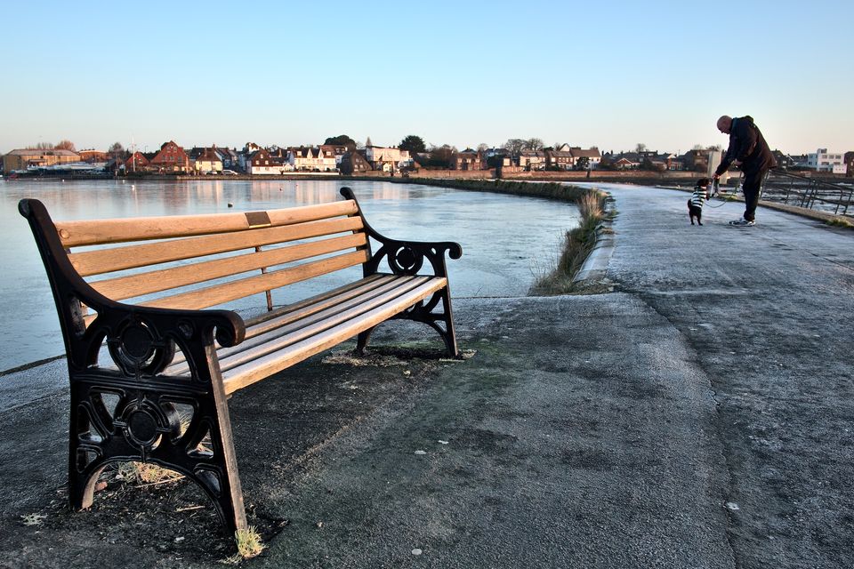 Frozen bench on Emsworth Quay with dog walker